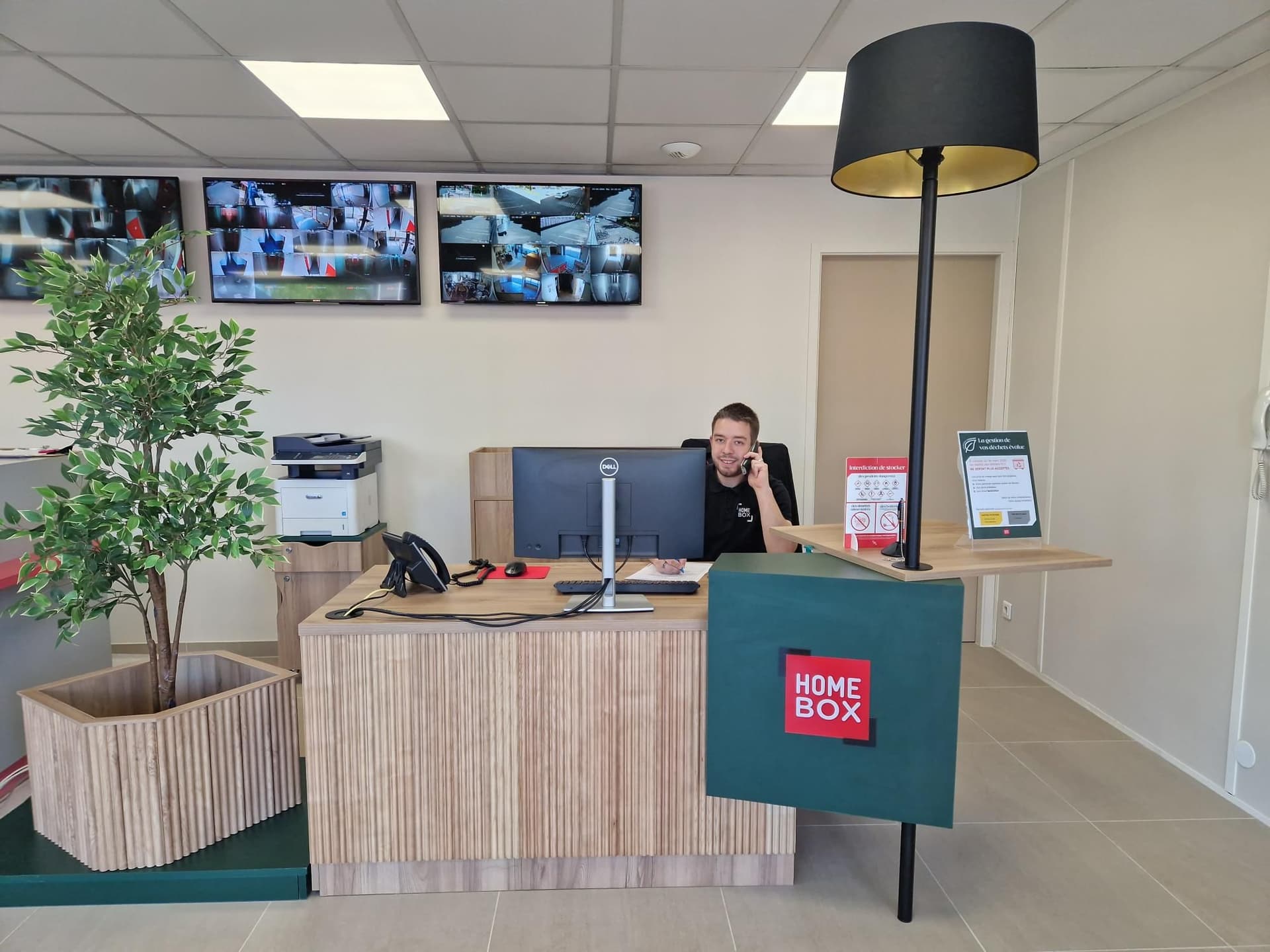 Conseiller au comptoir d'accueil avec écrans de vidéosurveillance muraux du centre HOMEBOX Linas Montlhéry
