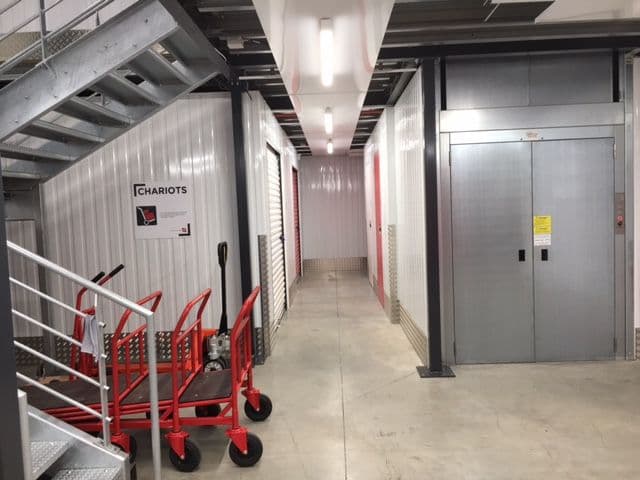 Hall intérieur avec chariots rouges, ascenseur et signalétique du centre HOMEBOX Tarbes
