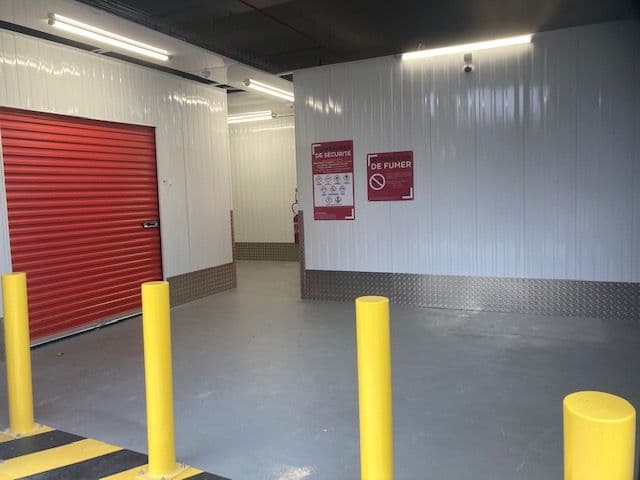 Zone de déchargement intérieure avec porte rouge, plots jaunes et panneaux de sécurité du centre HOMEBOX Toulon - Les Routes