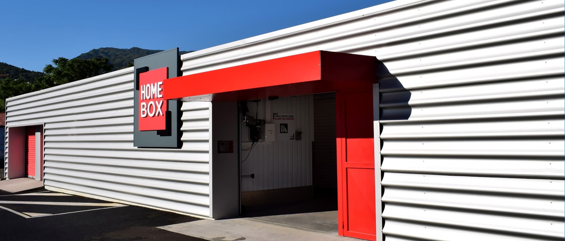 Façade blanche nervurée avec auvent rouge et logo HOMEBOX, HOMEBOX La Réunion, 40 rue Mahatma Gandhi à La Possession