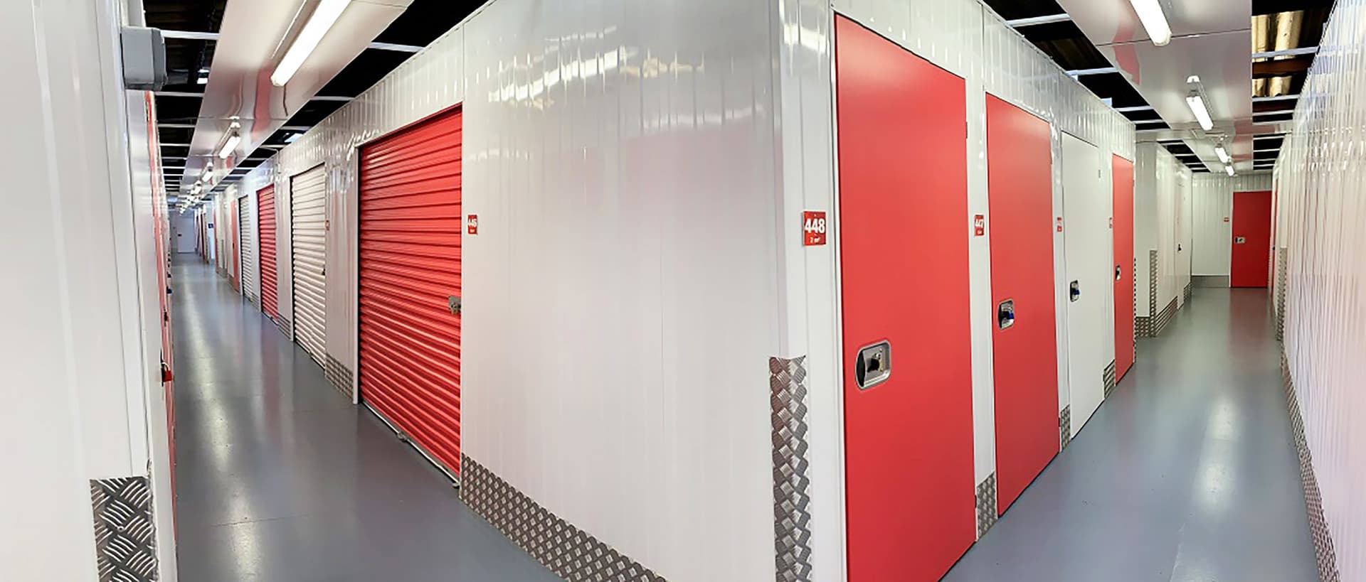 Couloir intérieur avec rangées de portes de boxes rouges et blanches du centre HOMEBOX Le Mans