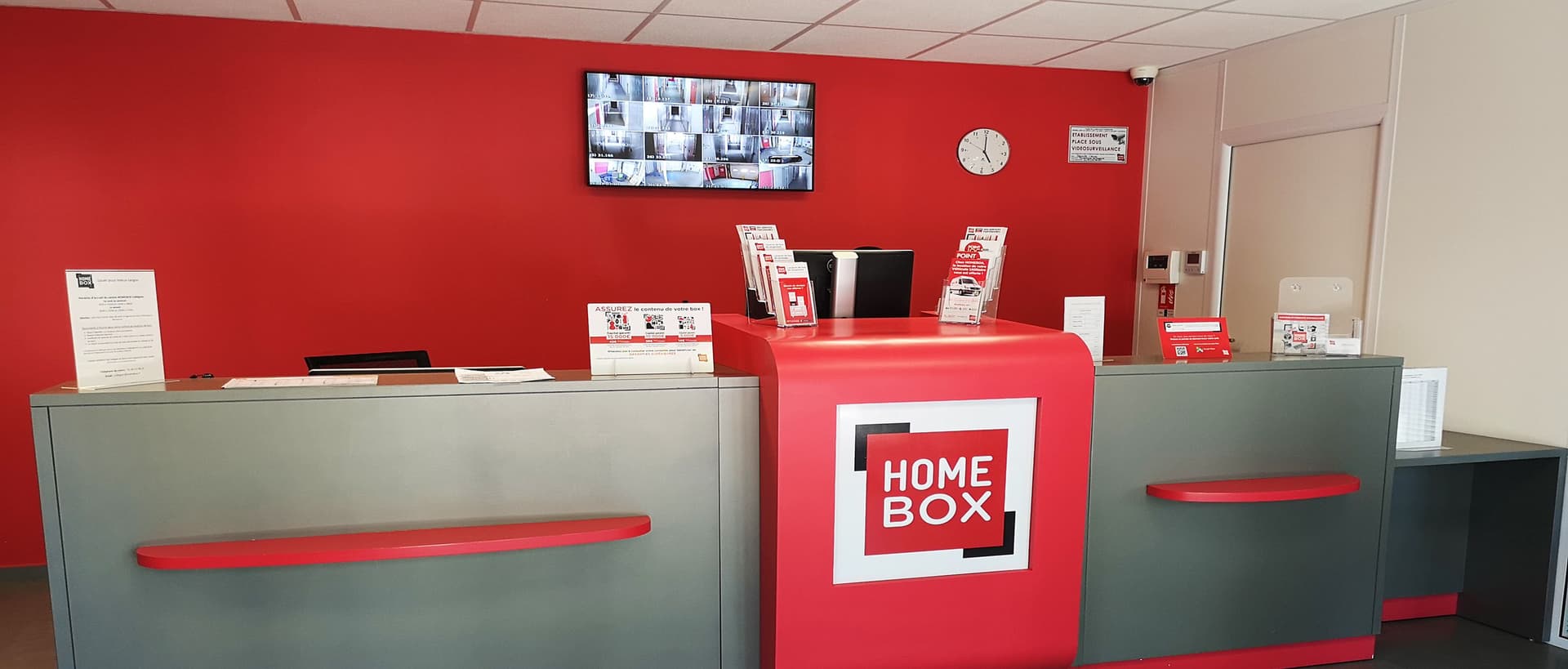 Comptoir d'accueil rouge avec logo et écrans de vidéosurveillance, HOMEBOX Strasbourg - Schiltigheim