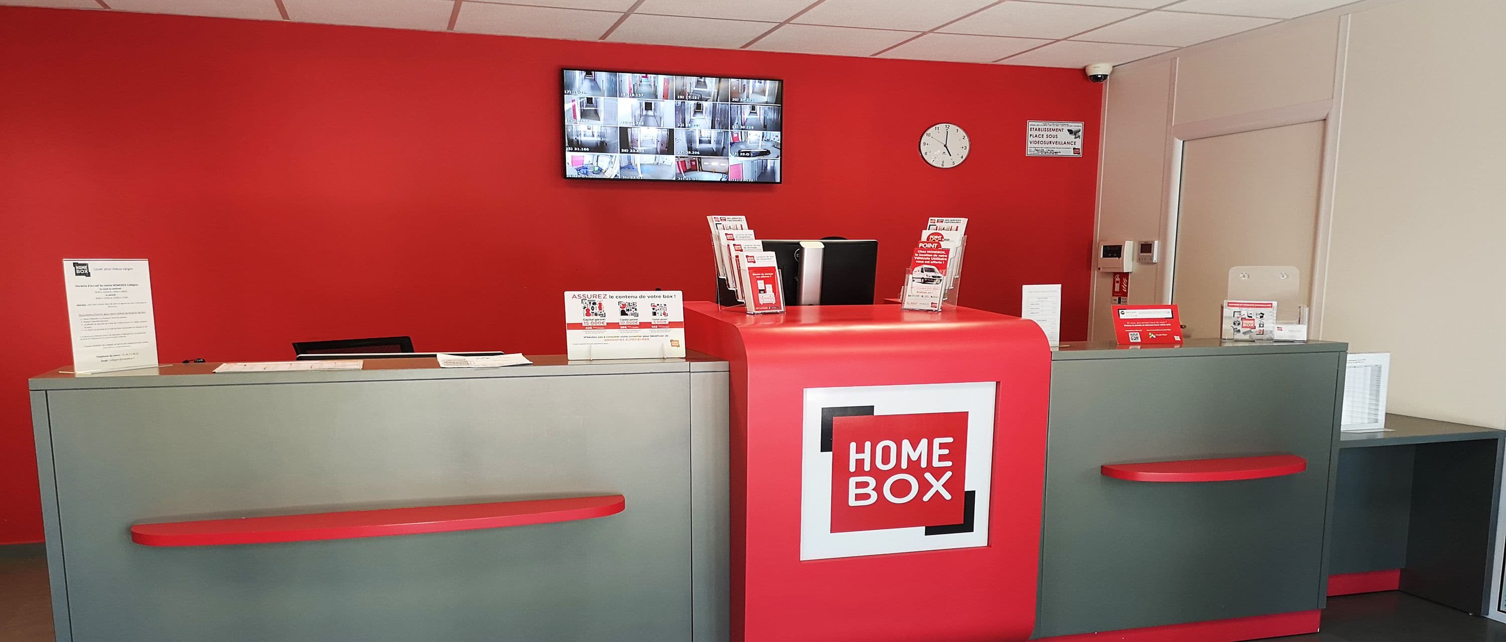 Comptoir d’accueil du centre HOMEBOX Angoulême avec mur rouge et écran de vidéosurveillance.