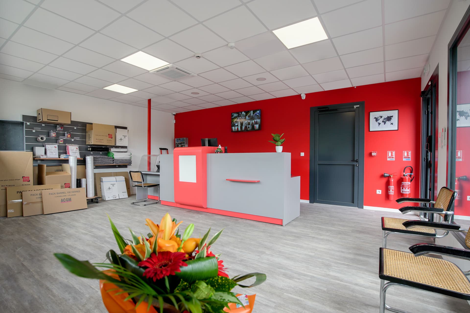 Comptoir d'accueil rouge et gris avec bouquet de fleurs et présentoir de cartons, HOMEBOX Saint-Gaudens