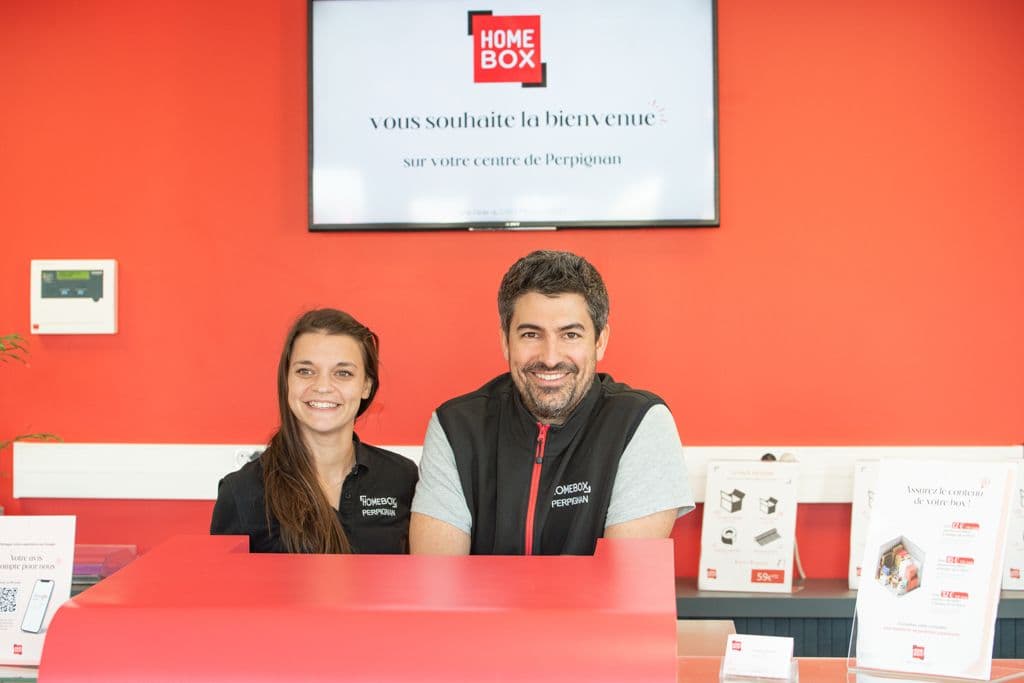 Équipe d'accueil souriante derrière le comptoir rouge du centre HOMEBOX Perpignan