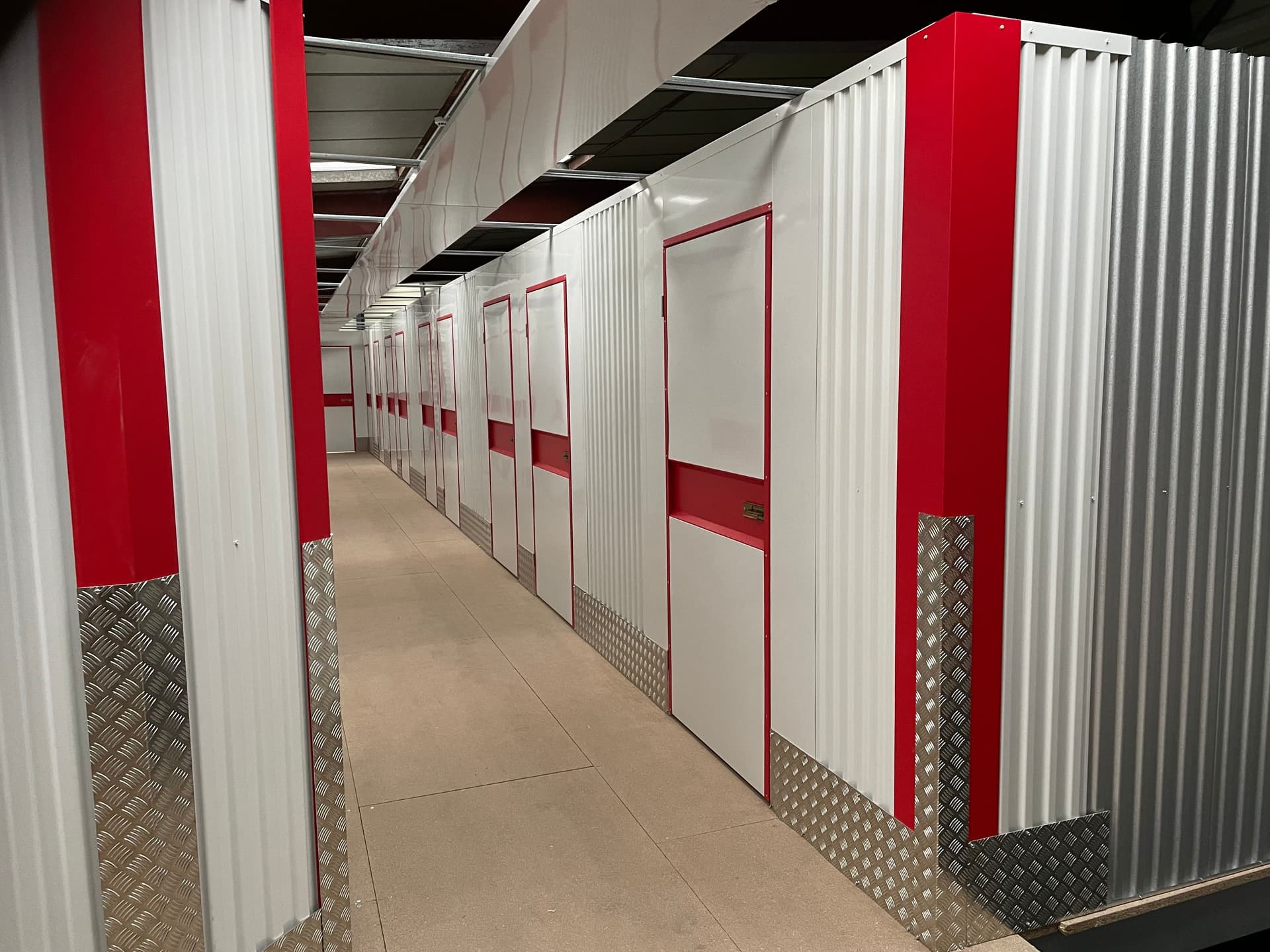 Allée intérieure étroite bordée de boxes rouges et blancs avec sol carrelé clair du centre HOMEBOX Saint-Marcellin