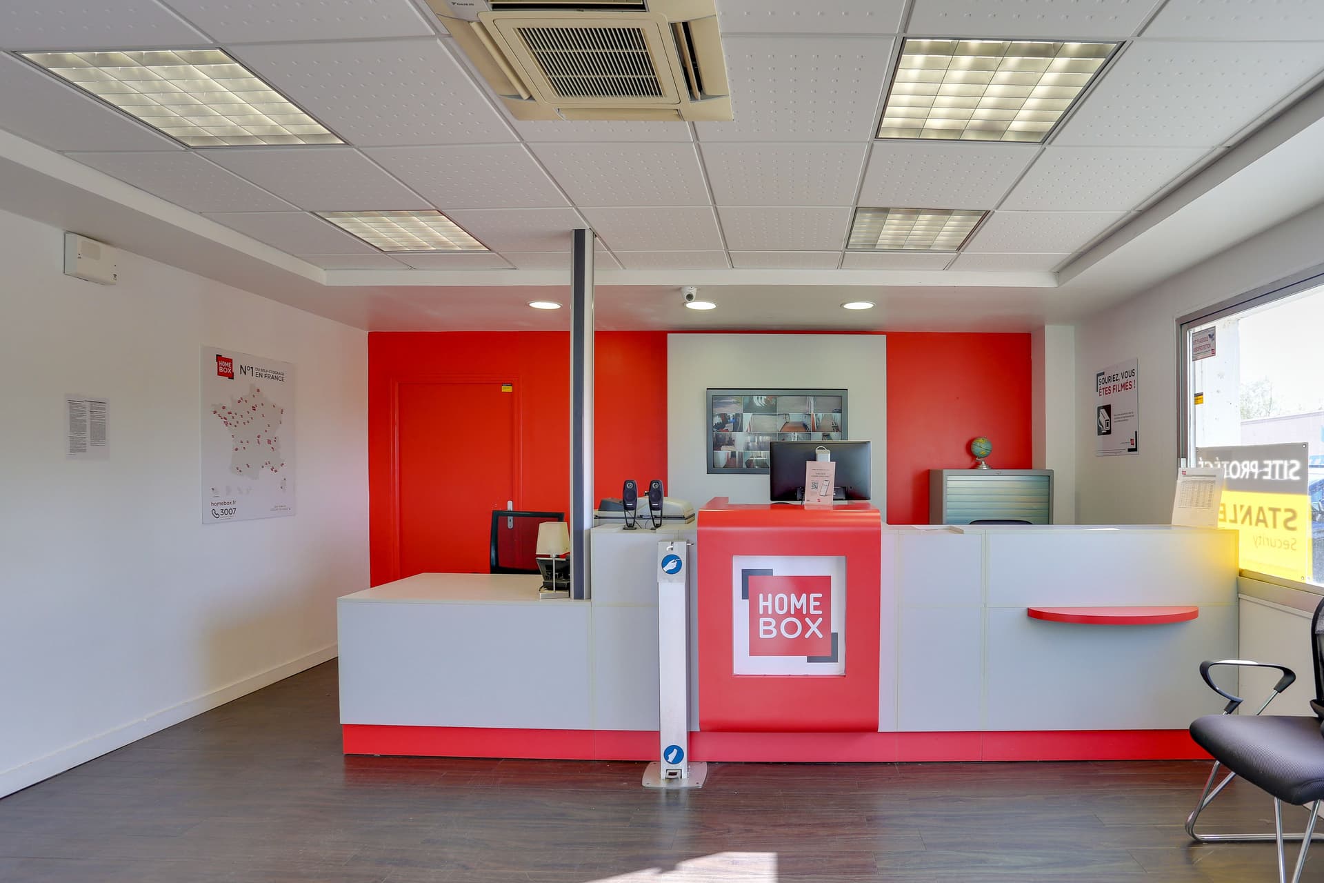Comptoir d'accueil rouge et blanc avec poste de travail et signalétique du centre HOMEBOX Rennes Sud