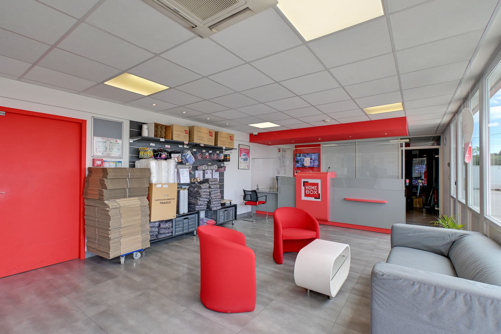 Espace d'accueil lumineux avec fauteuils rouges, comptoir et présentoir de cartons du centre HOMEBOX Les Pennes-Mirabeau