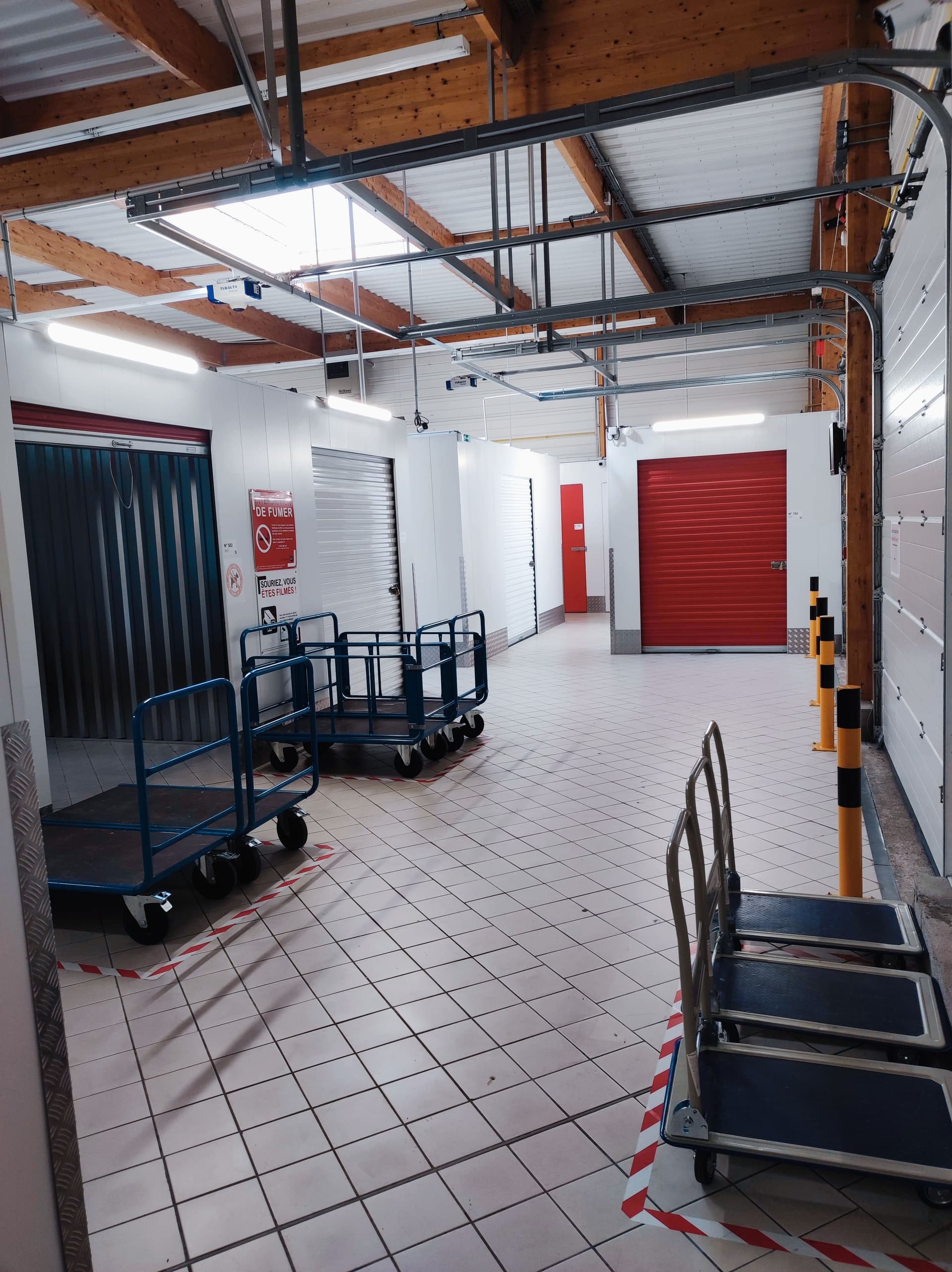 Zone de manutention avec chariots de transport et porte de garage rouge sous charpente bois du centre HOMEBOX Périgueux