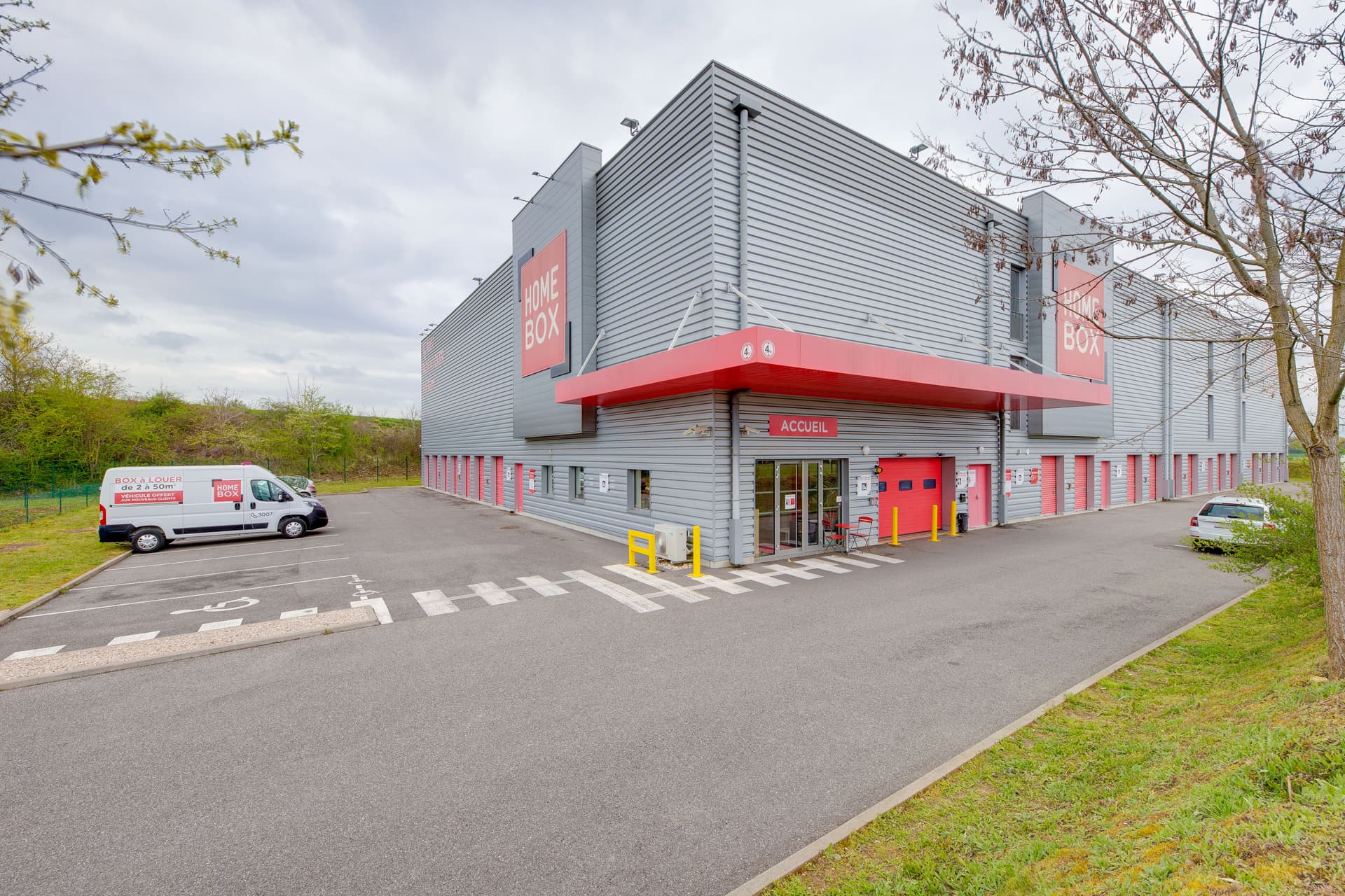 Vue d'ensemble du bâtiment gris et rouge avec parking et camionnette de location, HOMEBOX Mulhouse, 65 Rue de la rampe à Habsheim