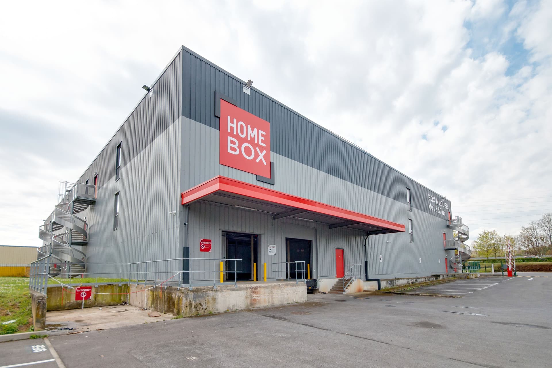 Façade d'angle gris et rouge avec enseigne HOMEBOX et auvent d'entrée, HOMEBOX Reims Sud, Rue William Shakespeare à Reims