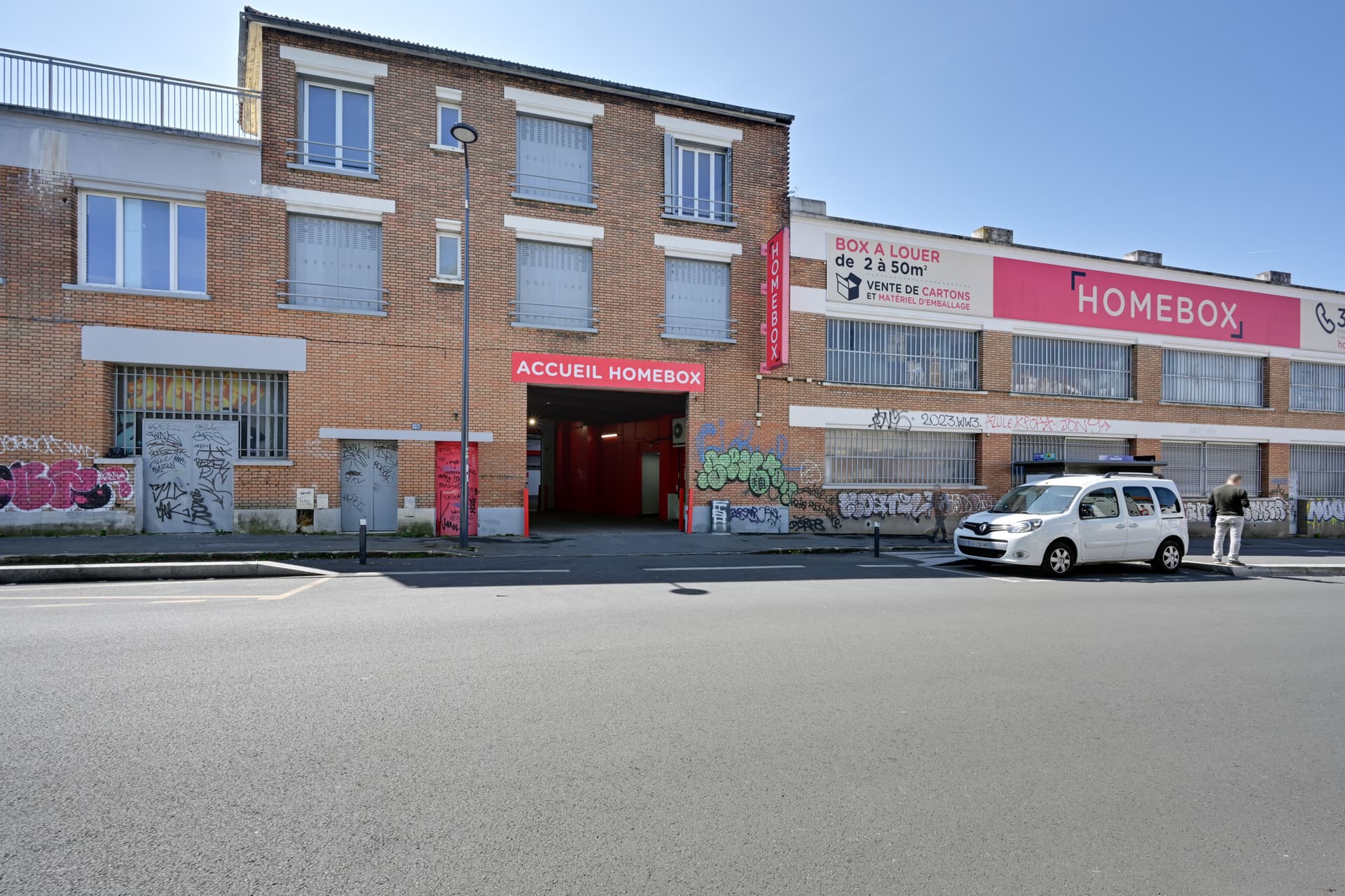 Vue large de la façade en briques avec porche d'entrée Accueil HOMEBOX et utilitaire blanc stationné, HOMEBOX Montreuil, 157 boulevard de Chanzy à Montreuil