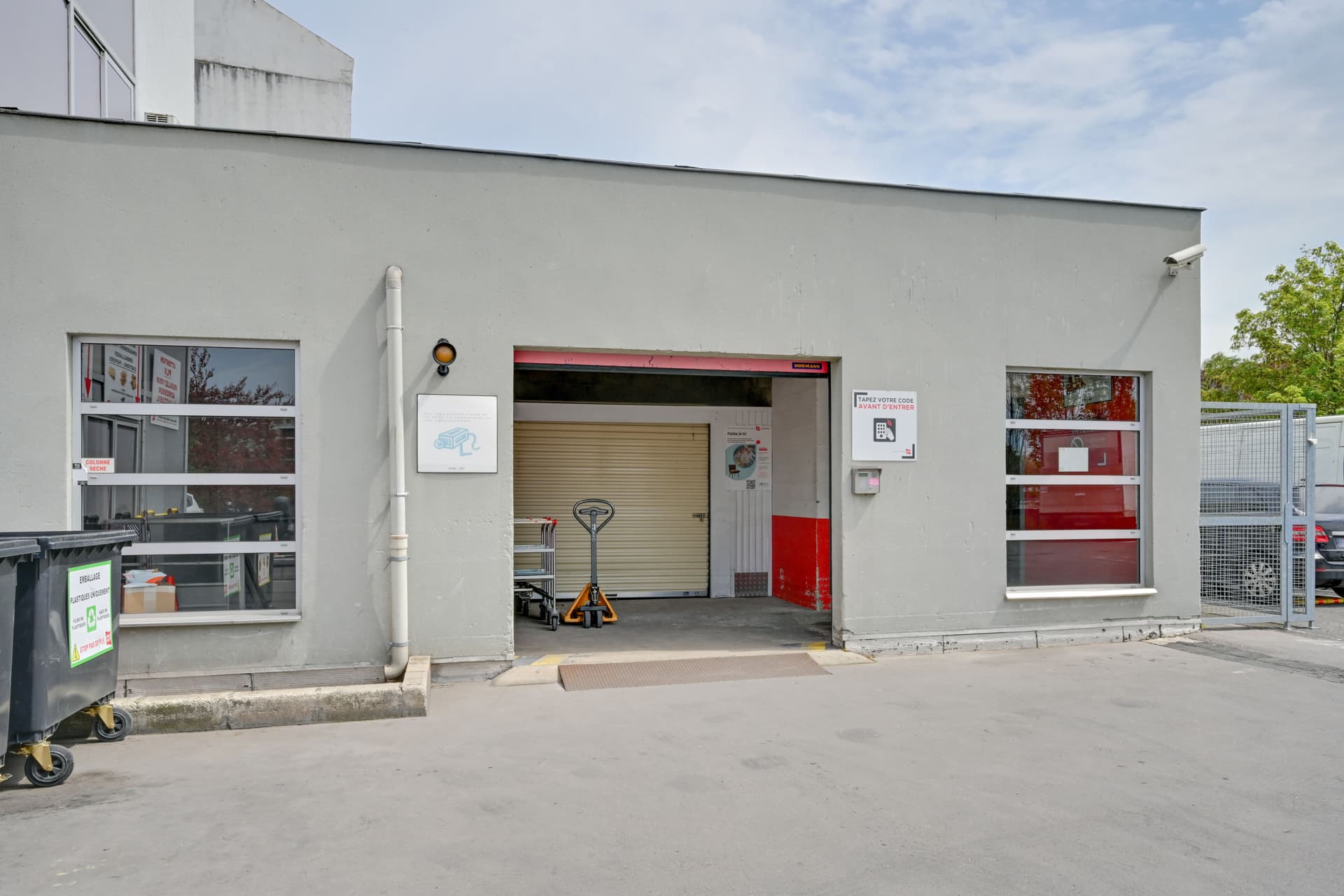 Entrée latérale grise avec rideau métallique ouvert et transpalette à l'extérieur, HOMEBOX Paris Porte de Bagnolet, 12-14 avenue de la République à Bagnolet