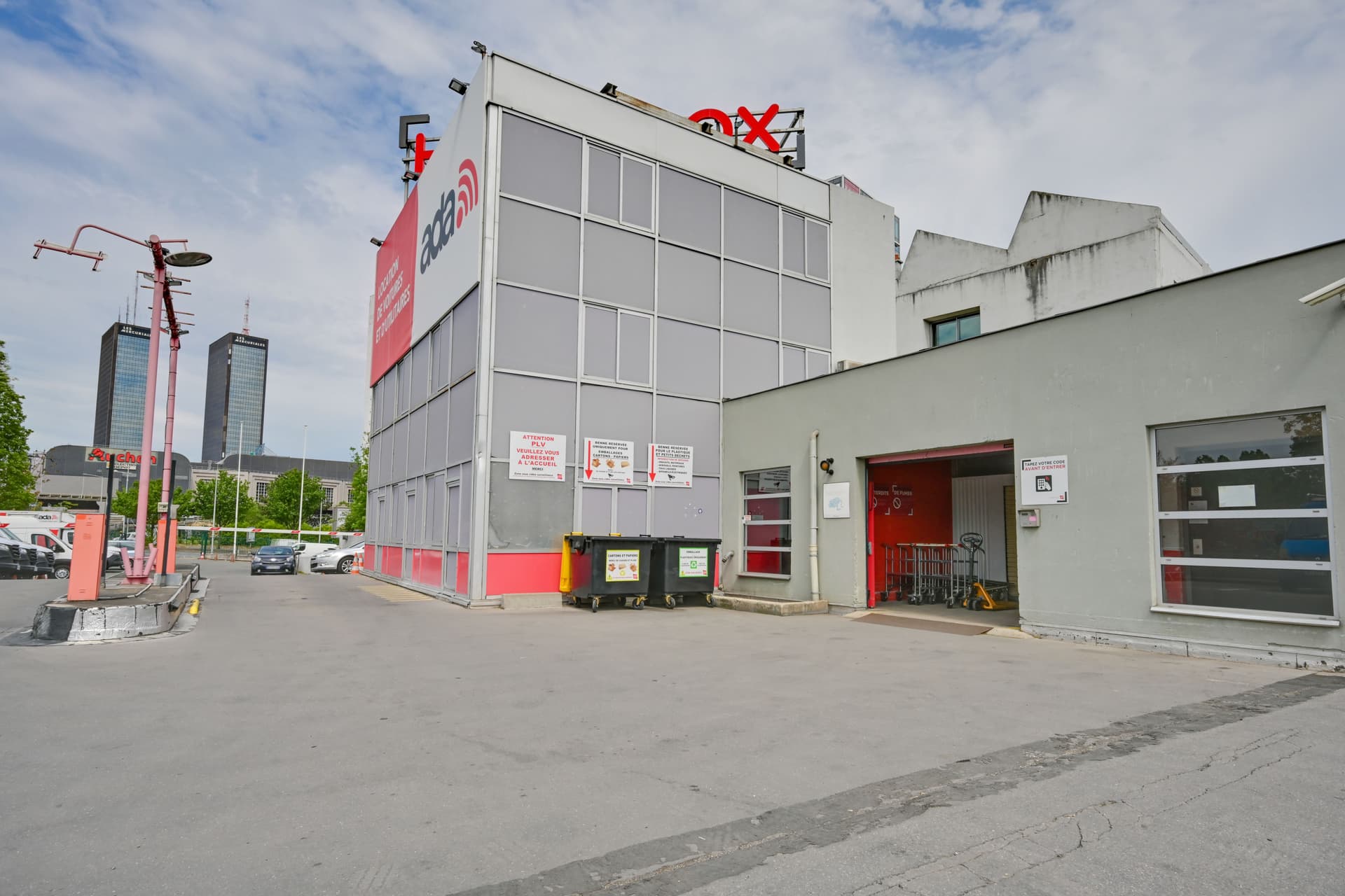 Façade arrière du centre avec bennes de tri et porte de service rouge sous ciel nuageux, HOMEBOX Paris Porte de Bagnolet, 12-14 avenue de la République à Bagnolet