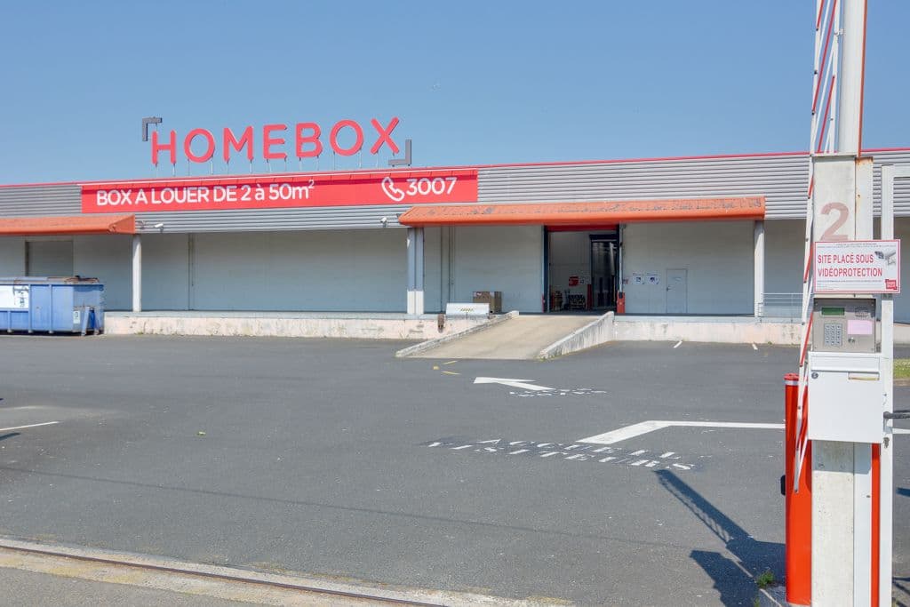 Façade blanche et rouge avec logo HOMEBOX et borne d'accès véhicule sous ciel bleu, HOMEBOX Nantes, 2 rue du Danemark à Carquefou