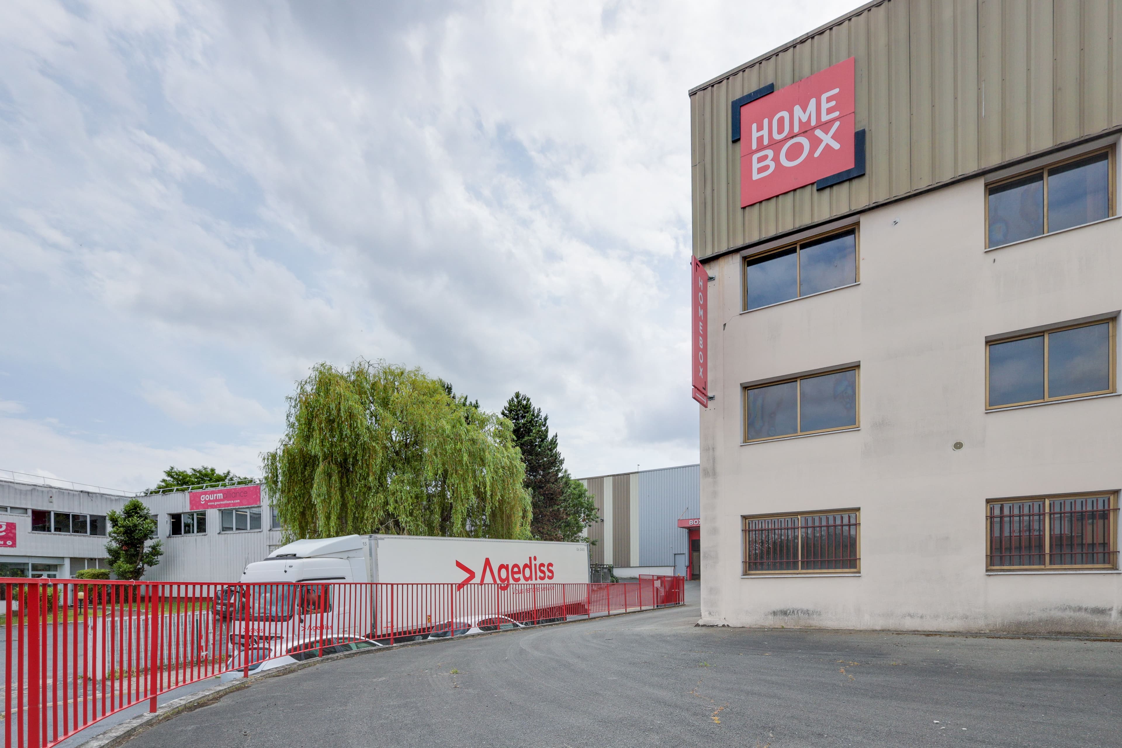 Façade du bâtiment Homebox avec enseigne et clôture rouge à l’entrée du centre de Franconville.