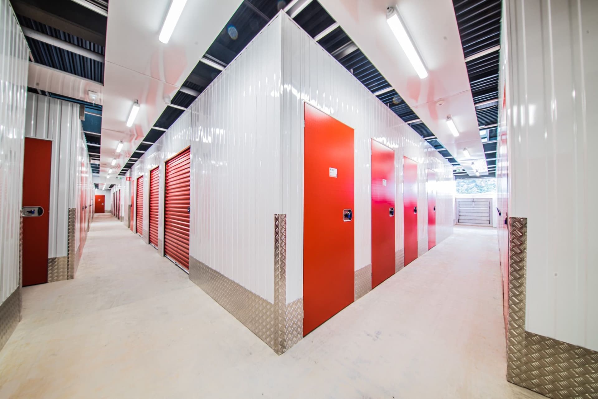 Couloir lumineux bordé de box aux portes rouges et blanches avec angles métalliques du centre HOMEBOX Thionville