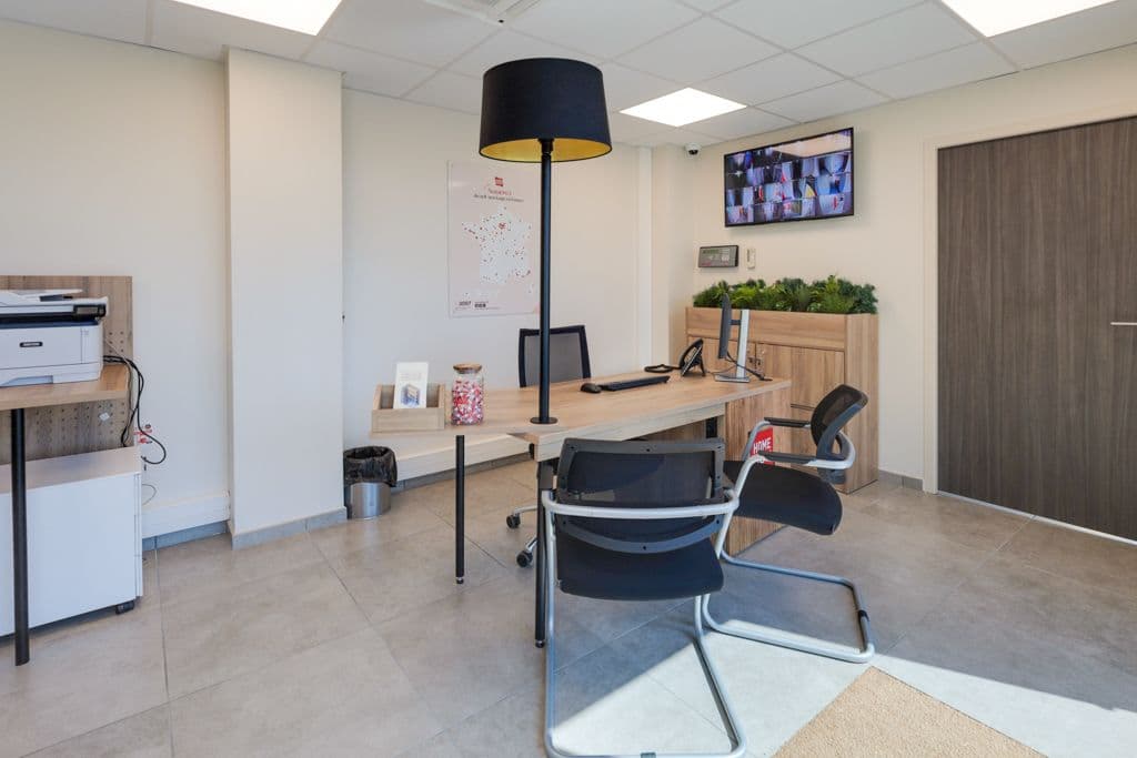 Bureau d'accueil avec mobilier bois, lampadaire noir et écran de vidéosurveillance du centre HOMEBOX Saint-Ouen-l'Aumône