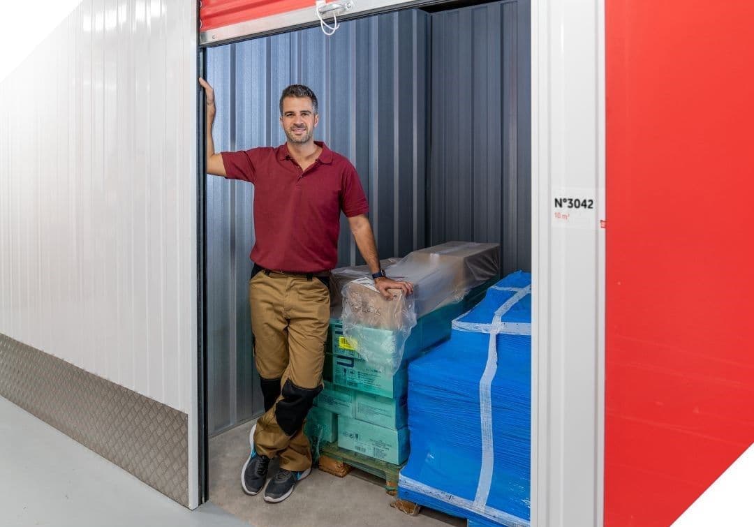 Client professionnel devant son box de stockage HOMEBOX rempli de cartons et matériel emballé, dans un couloir sécurisé.