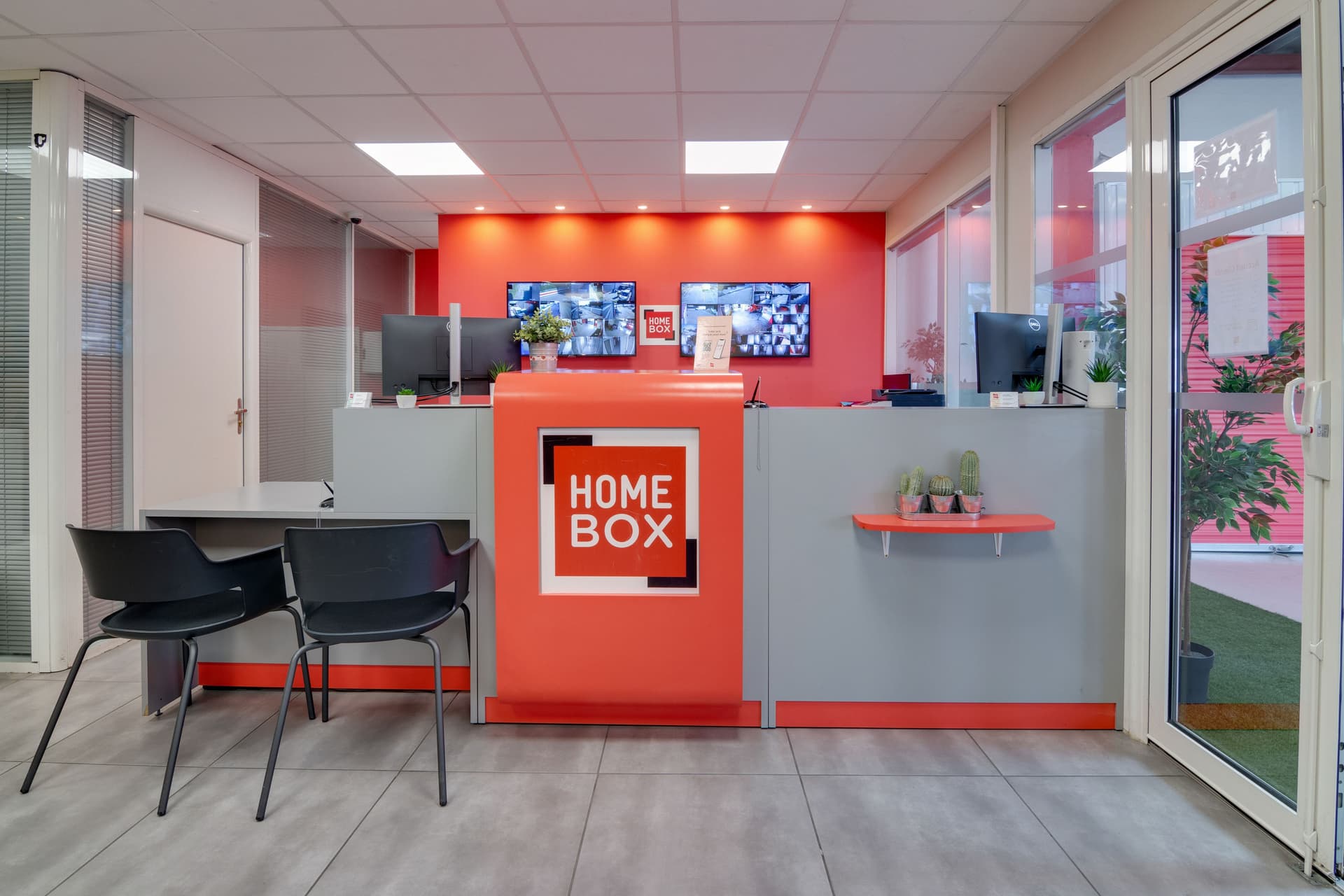 Espace d'accueil intérieur avec comptoir rouge logo HOMEBOX et écrans de vidéosurveillance du centre HOMEBOX Montpellier
