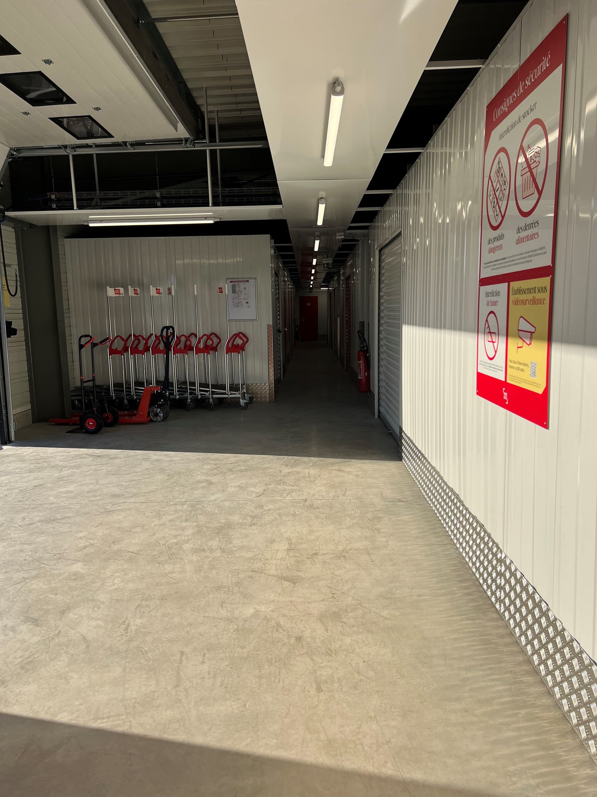 Couloir intérieur avec chariots de manutention alignés et affiches de sécurité du centre HOMEBOX Vitrolles