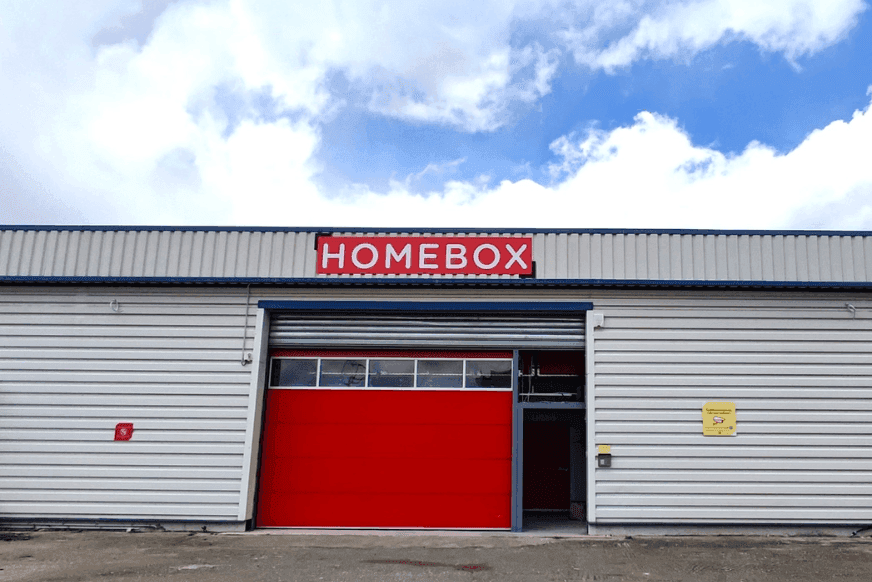 Façade du centre HOMEBOX Corte, 19C Zone d’activité artisanale, avec porte roulante rouge.