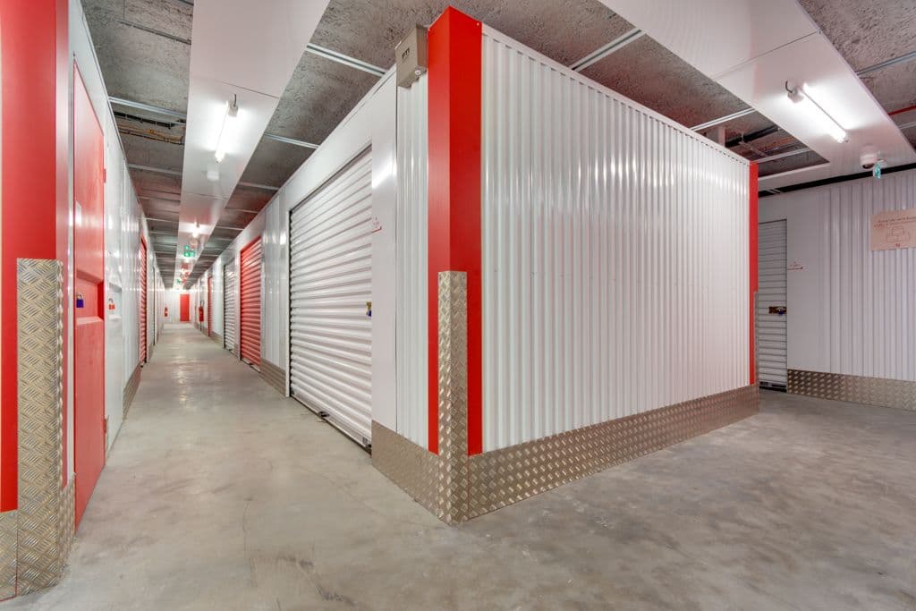 Couloir intérieur avec rangées de portes de boxes rouges et blancs et tôle striée au sol du centre HOMEBOX Lille La Pilaterie