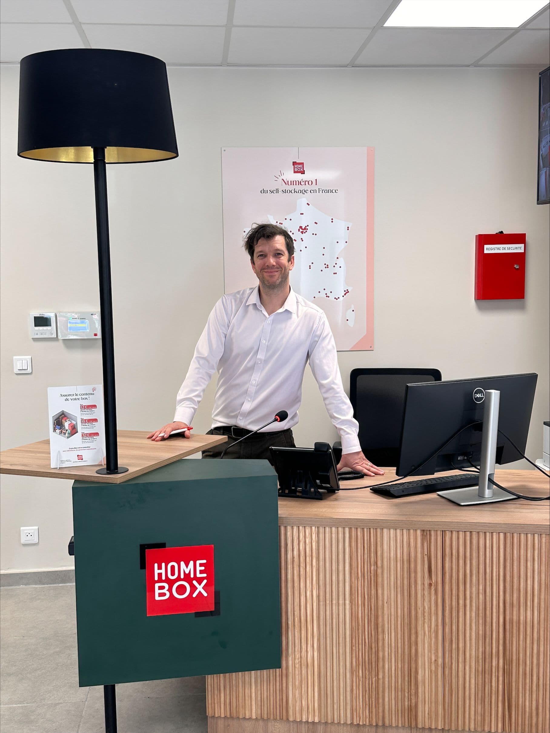 Conseiller souriant au comptoir d'accueil avec carte de France des centres du centre HOMEBOX Marseille - Le Rouet