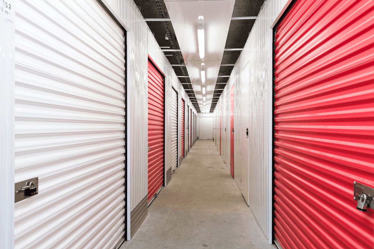 Couloir sécurisé d’un centre HOMEBOX avec alignement de box de stockage fermés par des portes rouges et blanches.