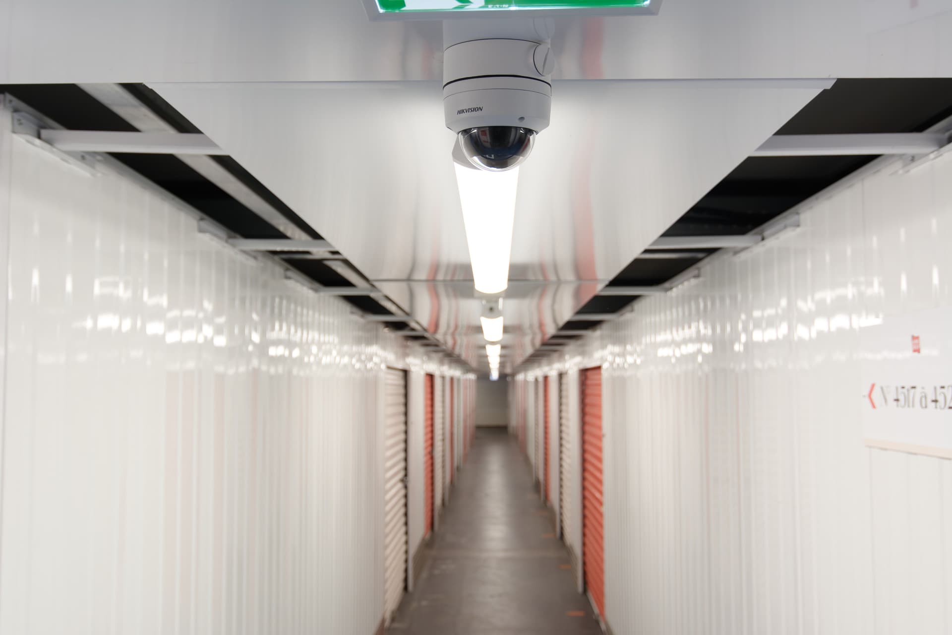 Couloir intérieur avec caméra de vidéosurveillance et rangées de boxes blancs, HOMEBOX Thonon-les-Bains